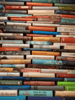 Das Bild zeigt eine Wand, an der unzählige Bücher zu einem hohen, dichtbepackten Bücherturm gestapelt sind.